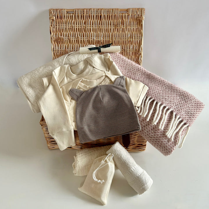 The St Andrews Hamper Company exclusive new baby wicker hamper filled with eco and organic clothes and accessories including a pure new wool baby blanket in dusky pink. 