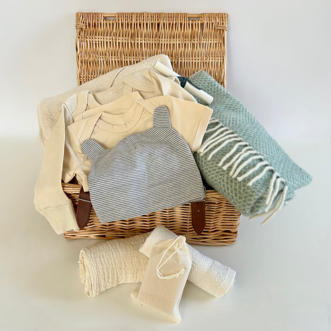 The St Andrews Hamper Company exclusive new baby wicker hamper filled with eco and organic clothes and accessories including a pure new wool baby blanket in ocean aqua.. 