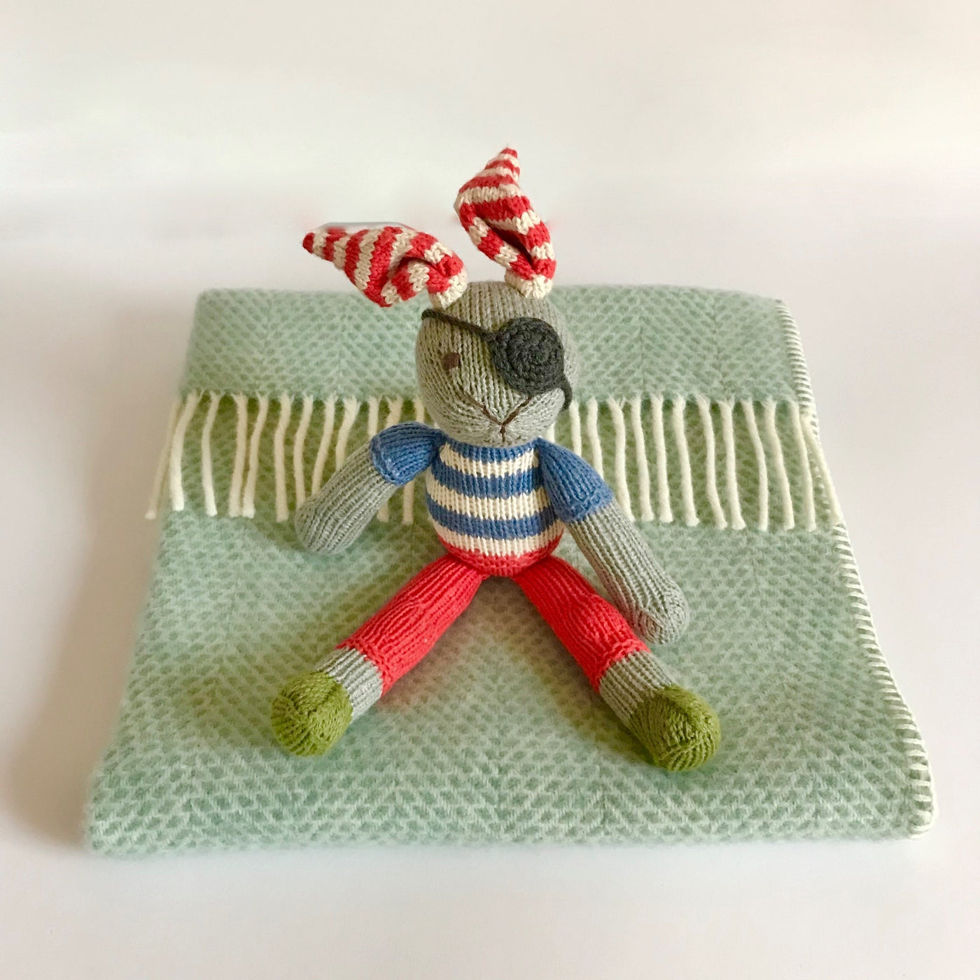Rory & Ruby pure new wool baby blanket in ocean aqua with organic cotton hand knitted pirate rabbit soft toy with red and white stripy ears and blue and white stripy jumper and an eye patch.